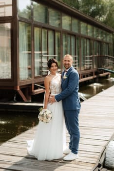 the first meeting of the bride and groom in wedding dresses on the pier near the water