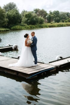 the first meeting of the bride and groom in wedding dresses on the pier near the water