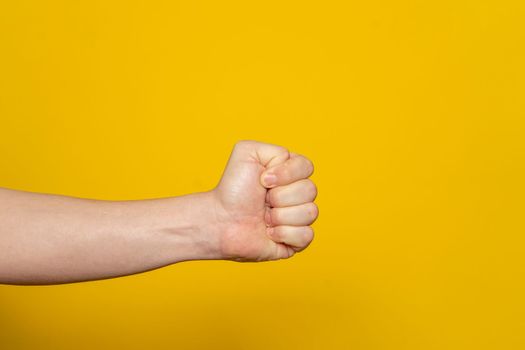 Strong man's hand in the form of a fist horizontally, isolated on yellow background. Fist ready to hit and hurt