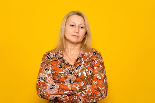 Caucasian blonde woman wearing a print dress angry with crossed arms isolated over yellow background. She is very upset by the different treatment received in her work compared to men.