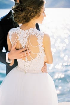 Groom put his hand on the back of the bride in a white dress. Back view. High quality photo