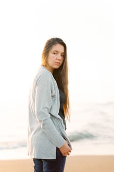 Girl in a sweater stands half-turned on the seashore. High quality photo