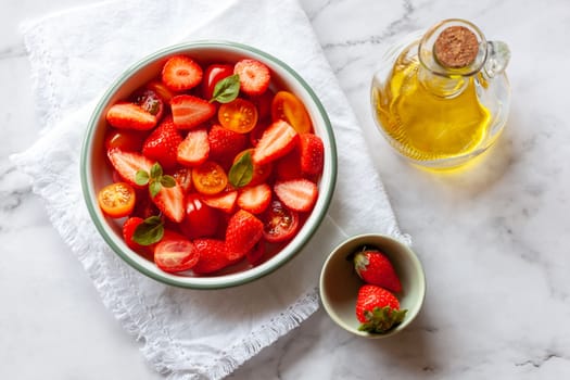 portion of strawberry and tomato cherry salad decorated with basil leaves, marble background, top view