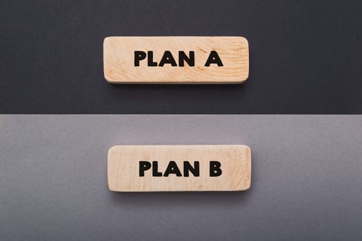 Phrases Plan A and Plan B on miniature wooden tablets on black and grey background upper view. Methods of achieving goals in business