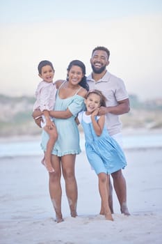 Full length portrait of a happy mixed race family standing together on the beach. Loving parents spending time with their two children during family vacation by the beach.
