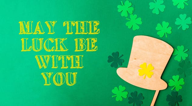 yellow motivational text May The Luck Be With You on a green background. the leprechaun's hat lies next to the clover leaves for good luck. Template for design, postcards, congratulations, etc.