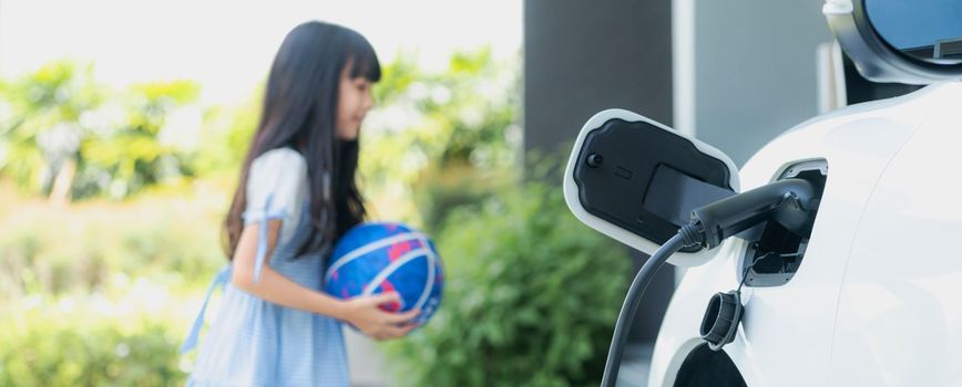 Focus home electric charging station for electric vehicle as alternative clean sustainable energy technology concept with blurred progressive young girl playing in the background at her home.