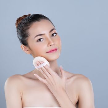 Glamorous beautiful female model applying cushion powder for facial makeup concept. Portrait of flawless perfect cosmetic skin woman put powder puff on her face in isolated background.