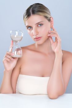 Alluring beauty model using hourglass in beauty concept of anti-aging skincare treatment for woman. Beautiful caucasian women portrait with perfect smooth clean skin in isolated background.