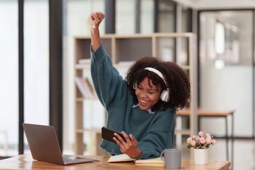 Excited Young black African woman wear headphone and enjoy with game via app on mobile phone