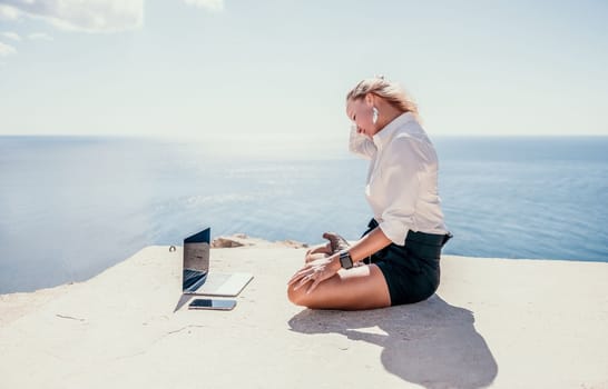 Happy girl doing yoga with laptop working at the beach. beautiful and calm business woman sitting with a laptop in a summer cafe in the lotus position meditating and relaxing. freelance girl remote work beach paradise