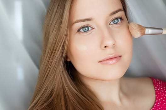 Beautiful woman applying liquid make-up foundation on her skin with make-up brush.