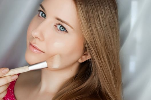 Beautiful woman applying liquid make-up foundation on her skin with make-up brush.