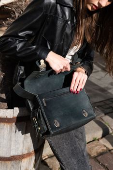 beautiful young girl with dark hair wearing jeans and a leather jacket posing outside with a leather bag