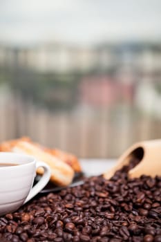 Coffee beans, sweet donut and a cup of coffee in close up photo