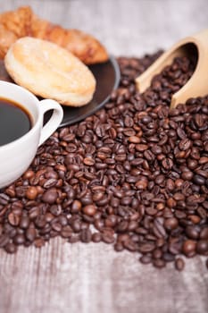 Coffee beans, donut and a cup of coffee in close up photo