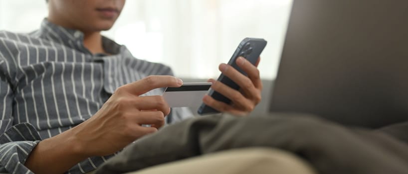 Young man holding credit cad and mobile phone, entering data for website form. E-commerce concept.