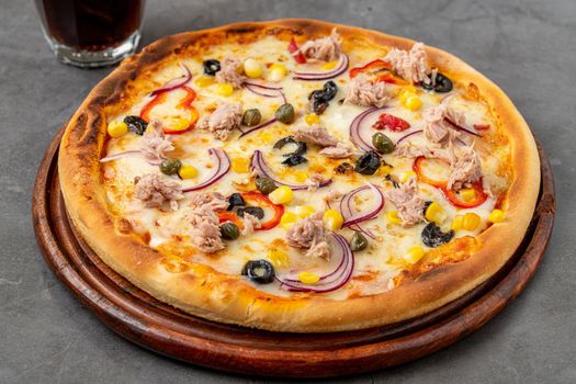 Pizza with tuna, onions and olives on cutting board on stone table