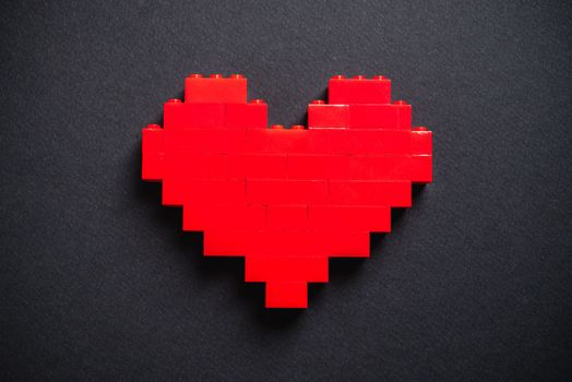 Red heart made of plastic bricks on a dark gray background