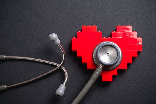 stethoscope standing on red heart on dark gray background