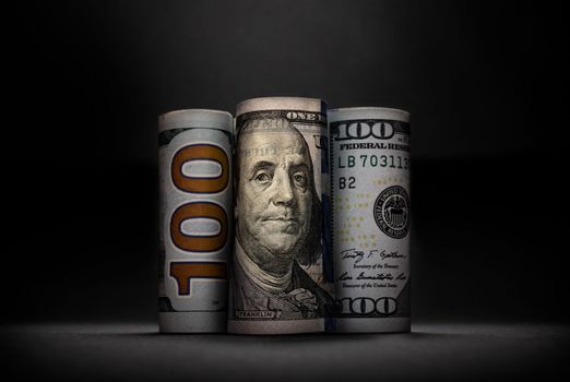 Three different images of 100 US dollars in rolls on dark background