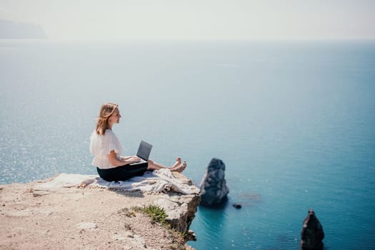 Successful business woman in yellow hat working on laptop by the sea. Pretty lady typing on computer at summer day outdoors. Freelance, travel and holidays concept.