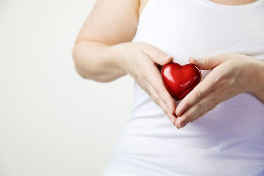 health, medicine and charity concept close up of female hands with small red heart holding for breast on white background copy space awareness