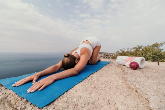 Middle aged well looking woman with black hair doing Pilates with the ring on the yoga mat near the sea on the pebble beach. Female fitness yoga concept. Healthy lifestyle, harmony and meditation.