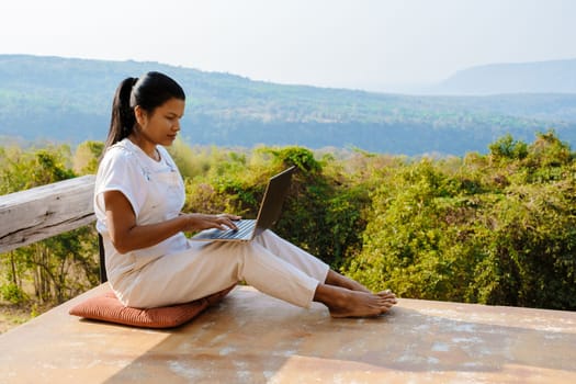 Young woman digital nomad traveler working online using a laptop and enjoying the beautiful natural landscape in front of a tent at sunrise. Digital nomad working on a laptop, remote working