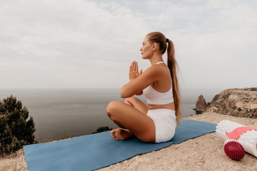 Middle aged well looking woman with black hair doing Pilates with the ring on the yoga mat near the sea on the pebble beach. Female fitness yoga concept. Healthy lifestyle, harmony and meditation.