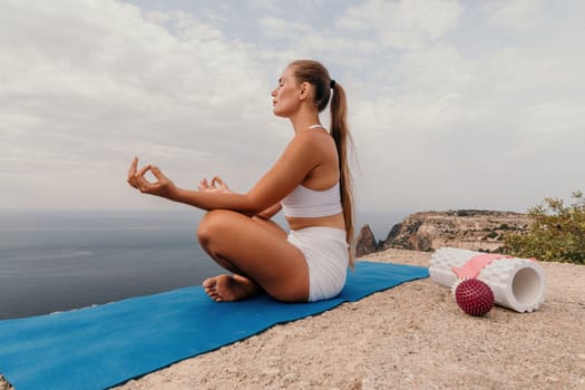 Middle aged well looking woman with black hair doing Pilates with the ring on the yoga mat near the sea on the pebble beach. Female fitness yoga concept. Healthy lifestyle, harmony and meditation.