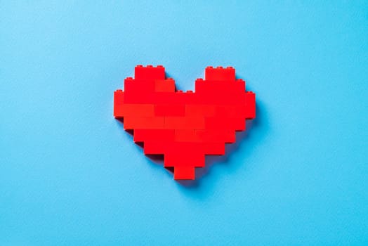 Red heart made of plastic bricks on a blue background