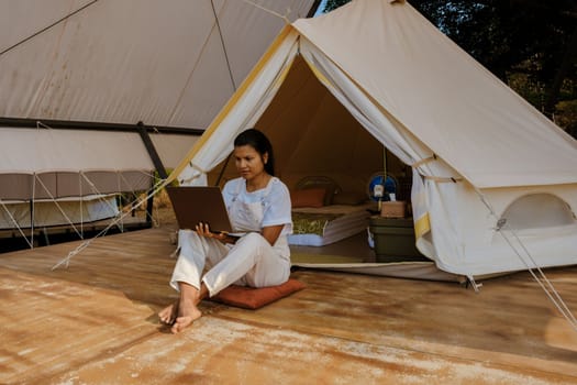 Young Asian woman freelancer traveler working online using a laptop and enjoying the beautiful natural landscape in front of a tent. Digital nomad working on a laptop, remote working