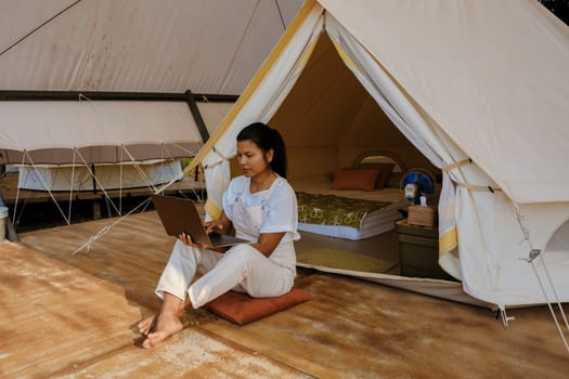 Young woman freelancer traveler working online using a laptop and enjoying the beautiful natural landscape in front of a tent. Digital nomad working on a laptop, remote working