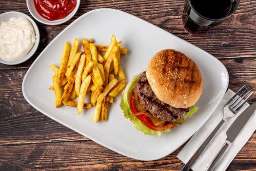 Delicious grilled homemade hamburger with beef, tomatoes, cheese, and lettuce on rustic wooden background