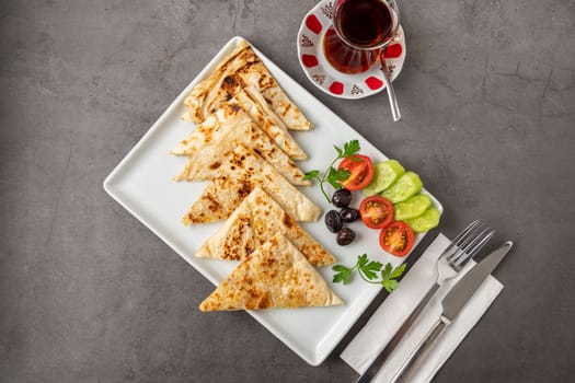 Traditional Turkish flatbread or Gozleme with tomatoes, olives and tea on dark stone table