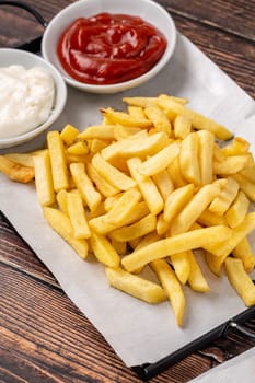 Golden French fries with ketchup and mayonnaise on wooden table