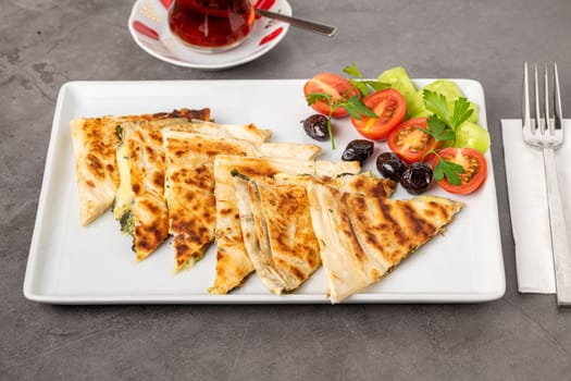 Traditional Turkish flatbread or Gozleme with tomatoes, olives and tea on dark stone table