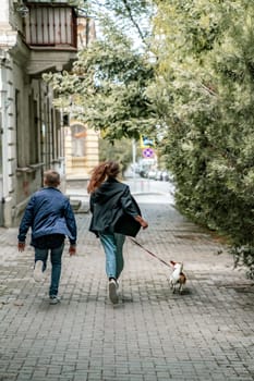 A girl and a boy are walking with a Jack Russell Terrier, walking down the street.