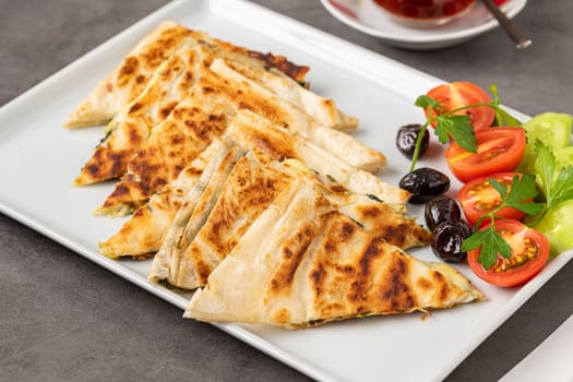 Traditional Turkish flatbread or Gozleme with tomatoes, olives and tea on dark stone table