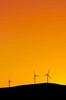 Multiple wind turbines standing on a hill at sunset and generating electricity