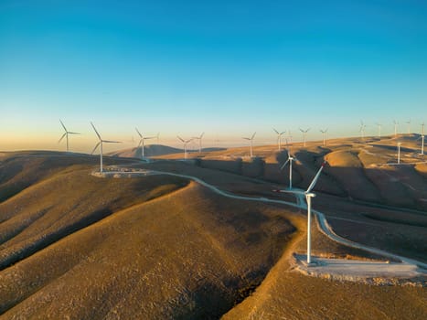 Aerial view of multiple wind turbines standing on a hill and generating electricity at sunrise