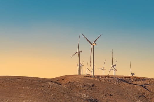 Multiple wind turbines standing on a hill at sunset and generating electricity