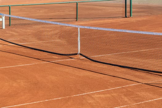 Baseline and net of an empty clay tennis court on a sunny day