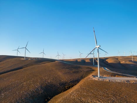 Aerial view of multiple wind turbines standing on a hill and generating electricity at sunrise