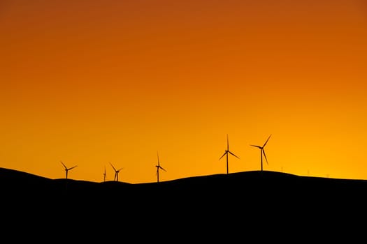 Multiple wind turbines standing on a hill at sunset and generating electricity