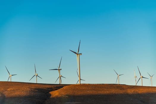 Multiple wind turbines standing on a hill at sunrise and generating electricity