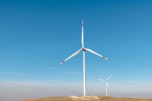 Multiple wind turbines standing on a hill at sunrise and generating electricity