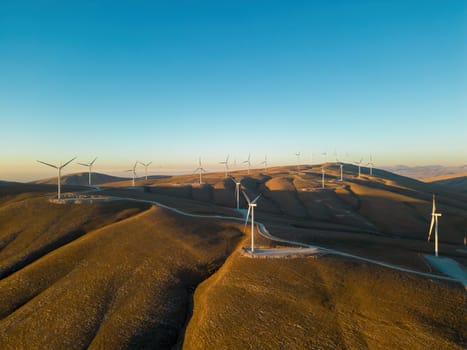 Aerial view of multiple wind turbines standing on a hill and generating electricity at sunrise