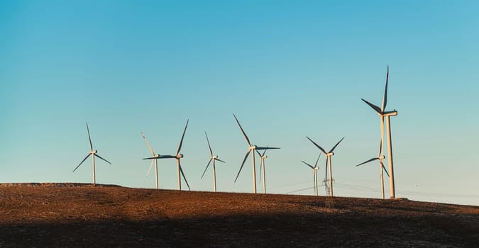 Multiple wind turbines standing on a hill at sunrise and generating electricity